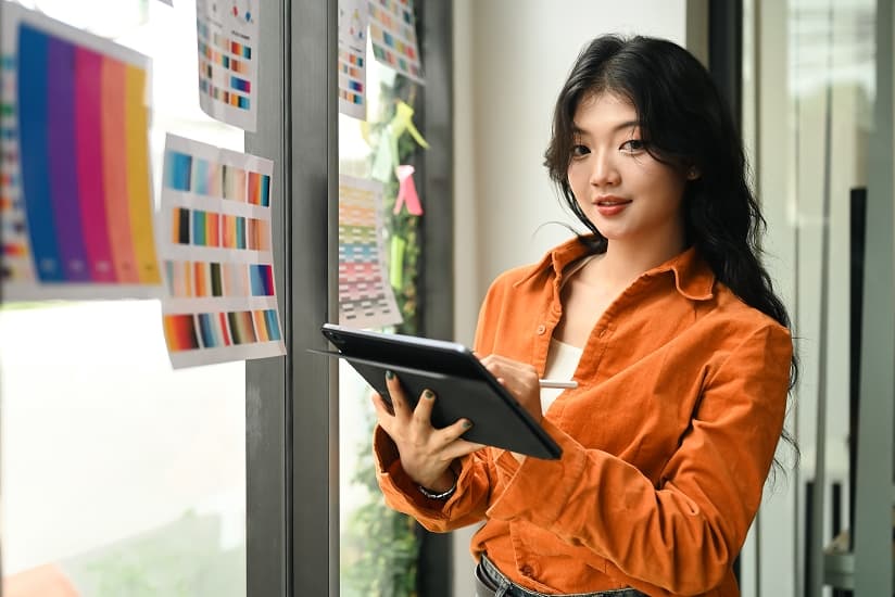 Une jeune femme créative choisissant un échantillon de couleur et portant une veste orange. 